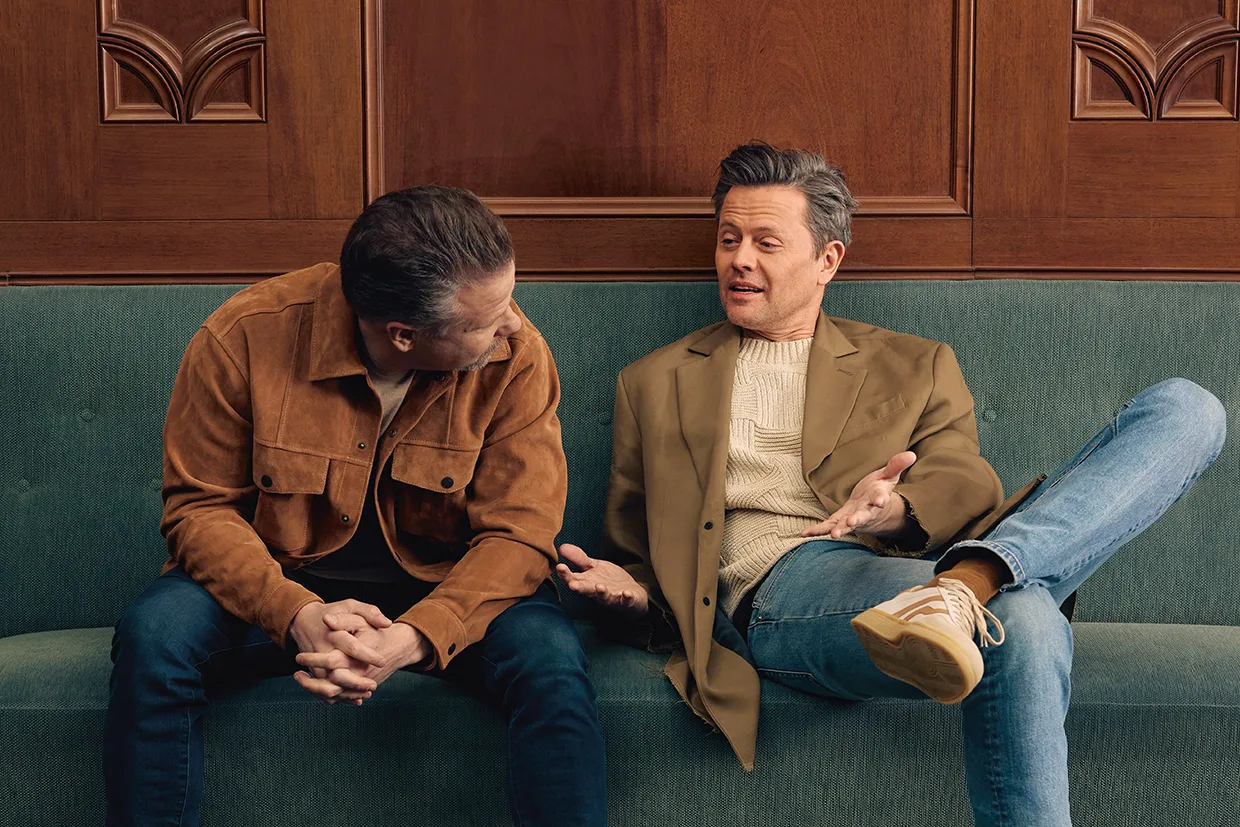 Filip och Fredrik sitter i en grön soffa och har ett avslappnat samtal. Den ene bär en brun kavaj och jeans och lutar sig framåt, medan den andre bär en brun kavaj, en ljus tröja och jeans och gestikulerar med händerna medan han talar.
