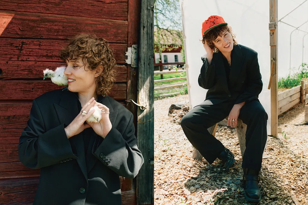 Amanda Bergman med lockigt hår i svart kostym håller en liten vit kyckling på axeln intill en röd trävägg (vänster) och sitter utomhus på en stubbe med en röd mössa och ler (höger).