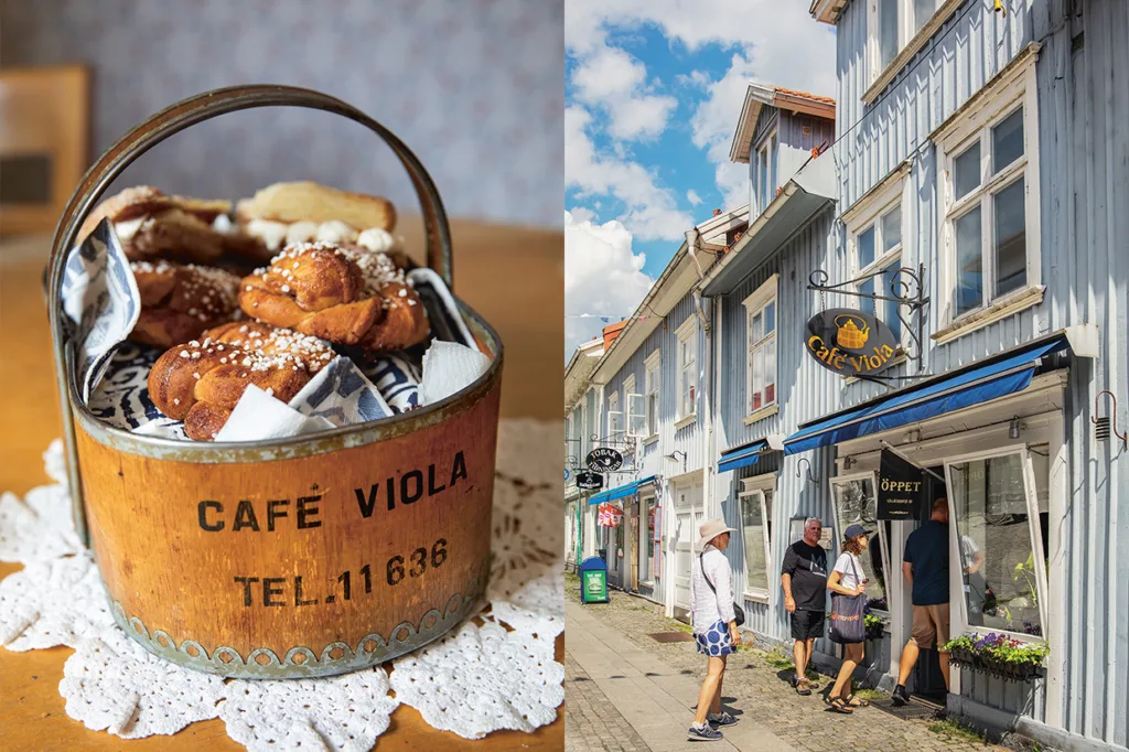En korg med texten Café Viola innehåller bakverk på en näsduk; bredvid korgen står människor utanför Café Viola, en blå träbyggnad med vita kanter under en delvis molnig himmel.