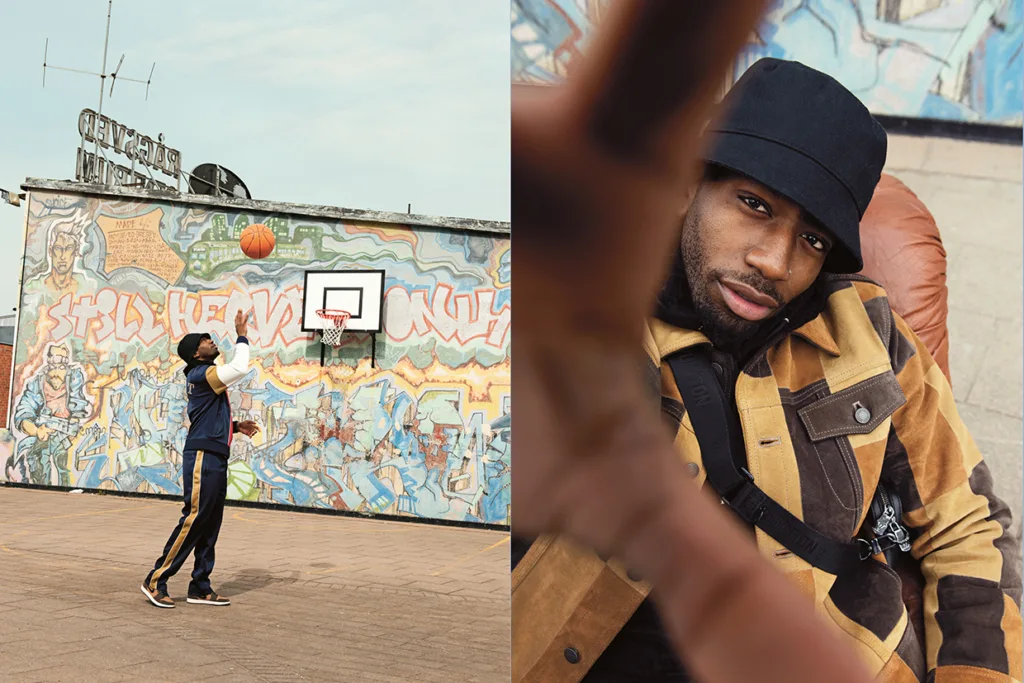 En man i hatt skjuter basketboll på en utomhusplan med graffitikonst på väggen; till höger sitter han på en stol och tittar in i kameran med handen utsträckt mot linsen.