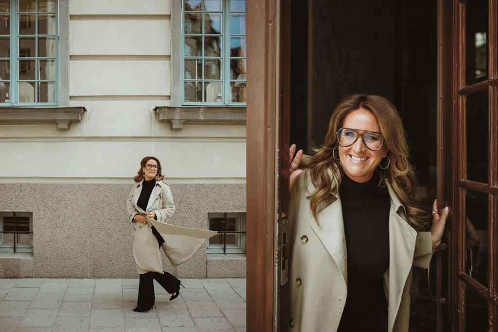 Denise Rudberg med långt brunt hår och glasögon bär en beige trenchcoat och svarta kläder. På det ena fotot går hon utomhus vid en byggnad, på det andra ler hon när hon står i en dörröppning.