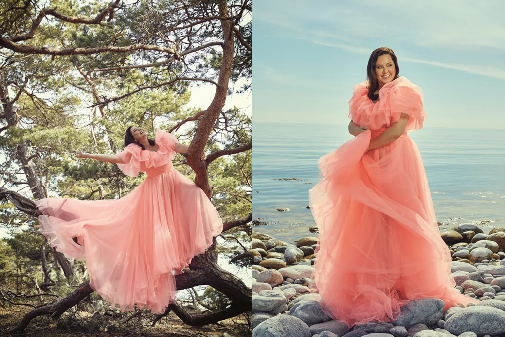 Viktoria Tocca i en böljande rosa klänning poserar i två miljöer: till vänster står hon på trädgrenar omgiven av grönska; till höger står hon på en klippstrand med havet och himlen i bakgrunden.
