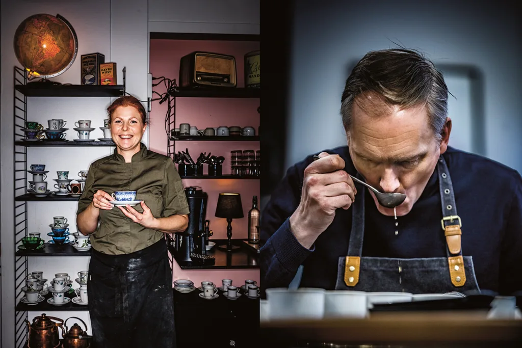 En kvinna ler på ett café och håller i en behållare med hyllor med koppar bakom sig. Bredvid henne smakar en man i förkläde på soppa ur en slev och fokuserar uppmärksamt.