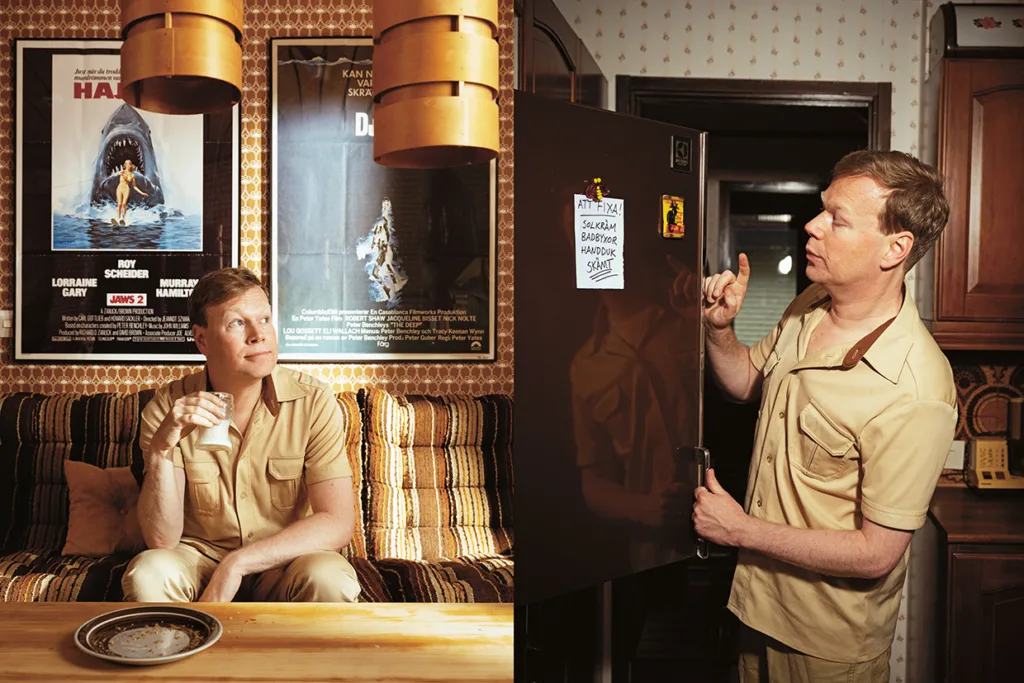 Johan Glans i solbränd klädsel befinner sig i ett rum i retrostil. Till vänster sitter han i en randig soffa och håller i ett mjölkglas, med Jaws-affischer i bakgrunden. Till höger pekar han på anteckningar på ett svart kylskåp.