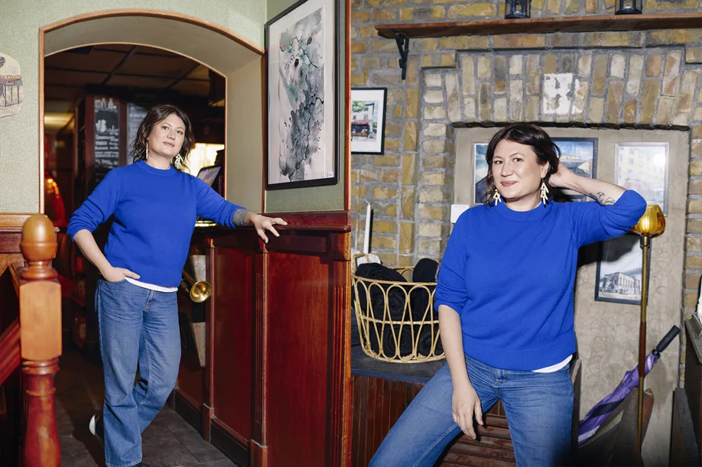 Två bilder: (t.v.) Ina Lundström klädd i blå tröja och jeans, poserar självsäkert, lutar sig mot en vägg i ett mysigt rum med träpanel och en öppen spis i sten. På den andra sitter hon på en bänk, ler.