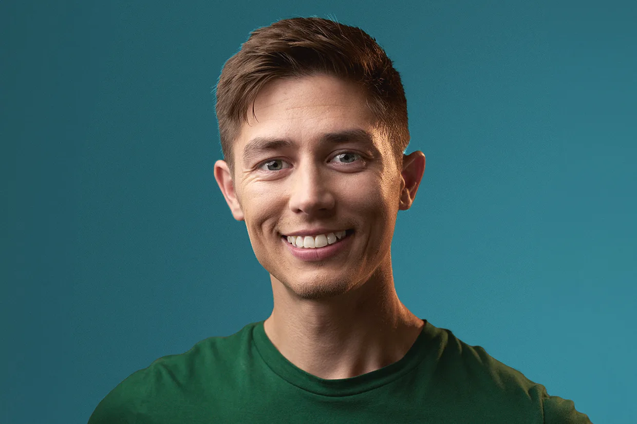 Alexander Hermansson med kort brunt hår och blå ögon, klädd i en grön t-shirt, ler mot kameran mot en blågrön bakgrund.
