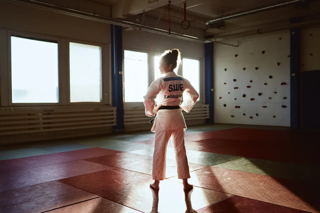 Tara Babulfath i judodräkt står på en matta i ett solbelyst gym, vänd bort från kameran. På ryggen av uniformen står det SWE och Babulfath.