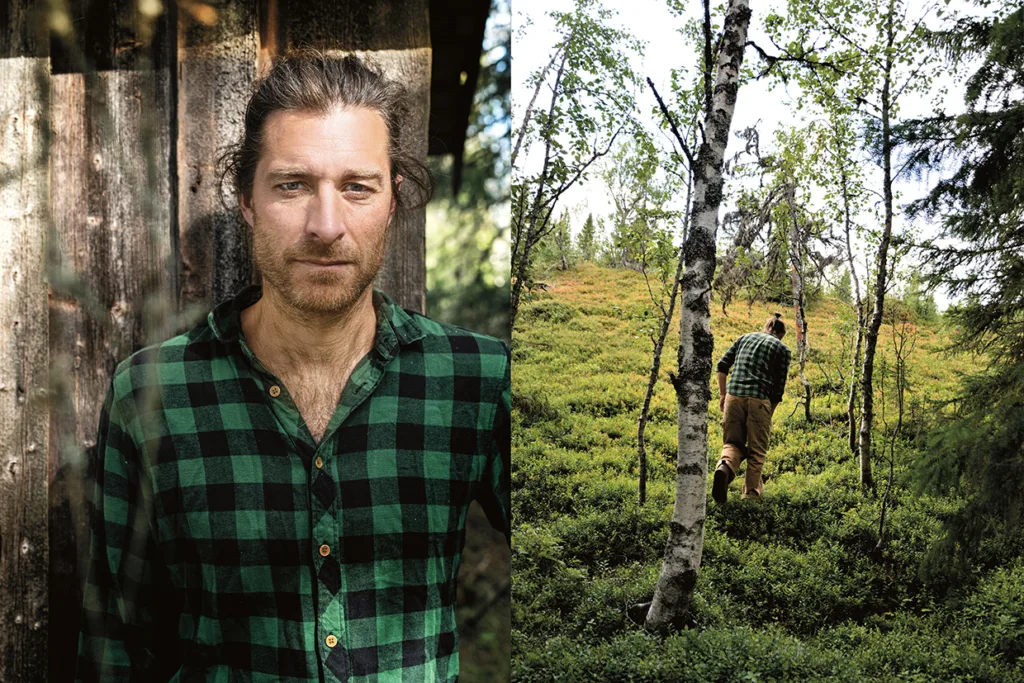 En man i grönrutig skjorta står vid en trävägg till vänster; till höger går han genom en grönskande skog med björkar och buskar, fotograferad bakifrån.